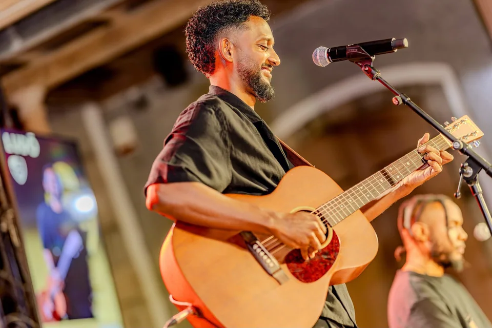 LUDŌ sur scène, jouant de la guitare acoustique au micro