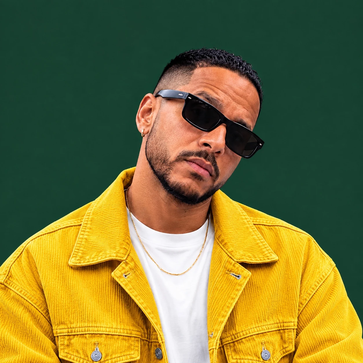 Portrait de YAMALO en veste jaune et lunettes noires sur fond vert profond